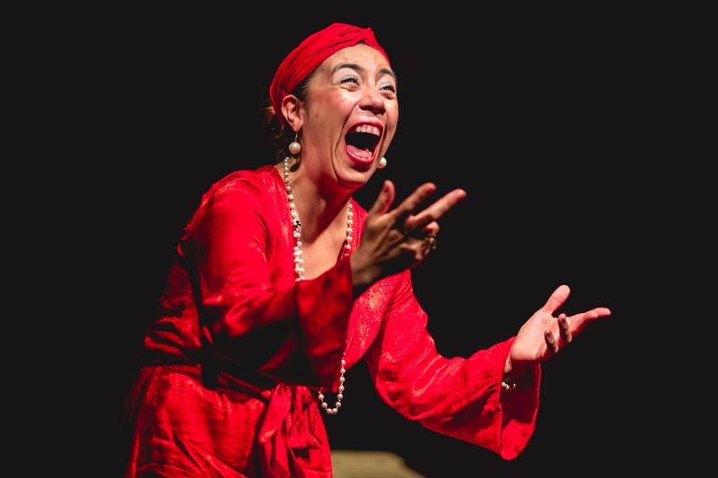 Escena de Pretexto. Una actriz vestida de rojo, en primer plano.