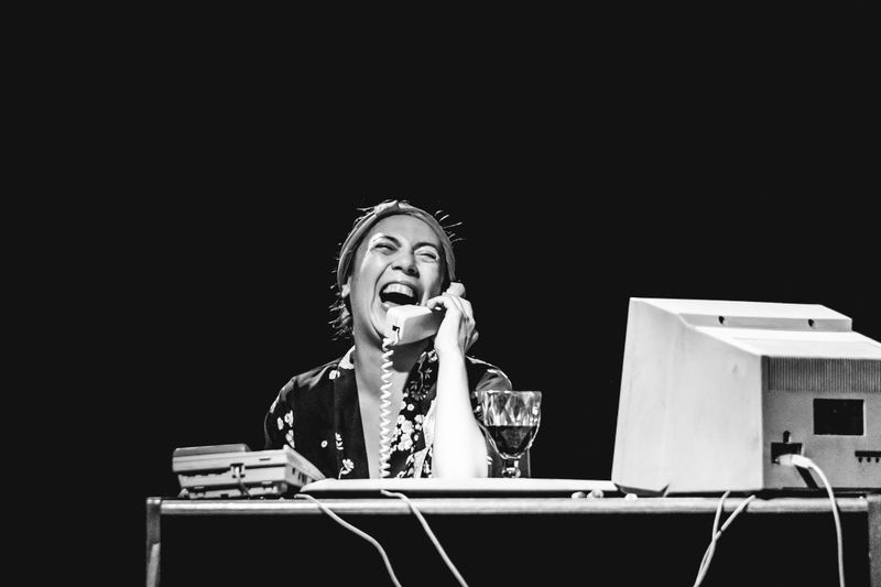 Escena de Pretexto en blanco y negro. Una actriz al teléfono junto al computador.